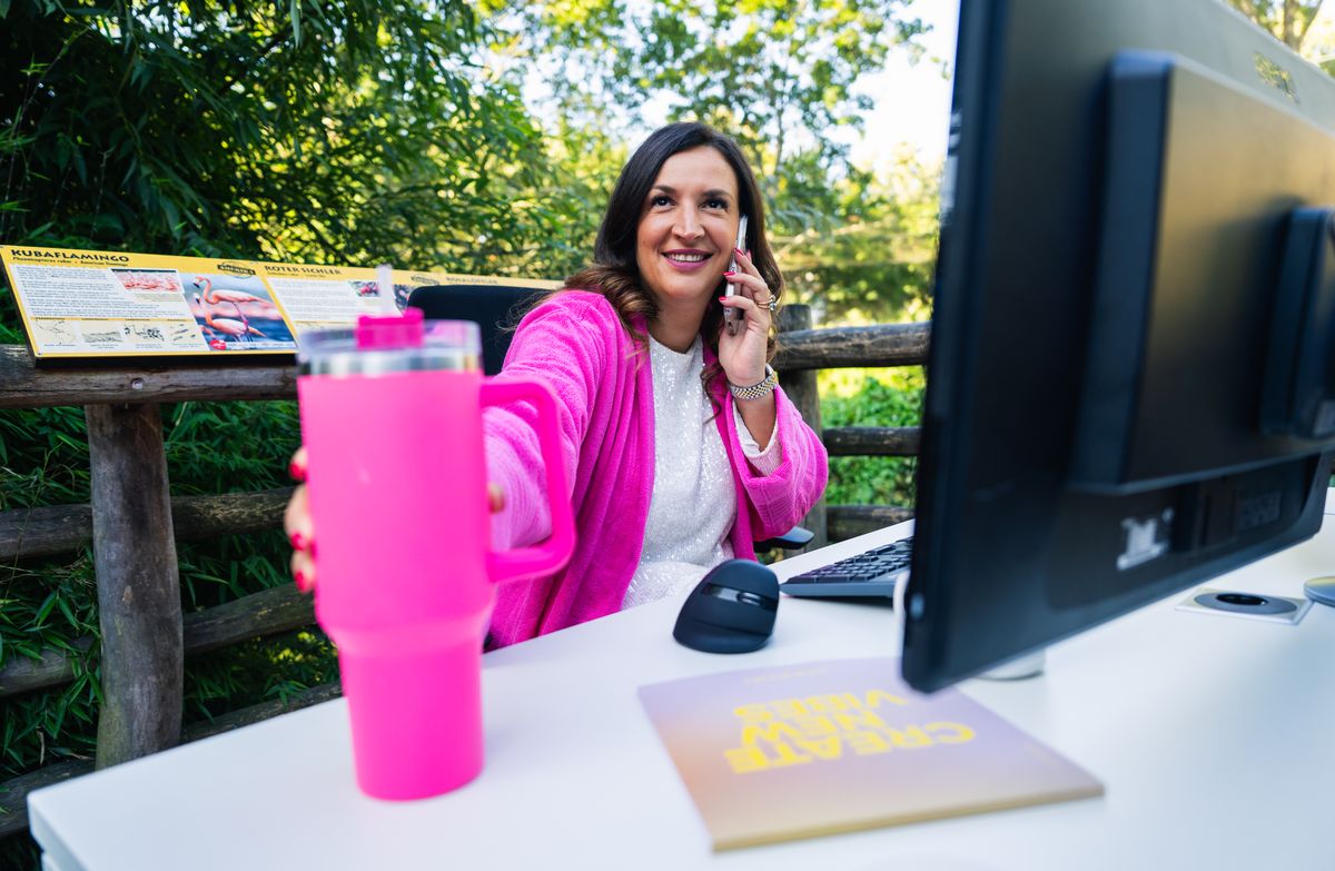 Frau telefoniert an einem wei&szlig;en Schreibtisch mit Monitor direkt am Zoogehege
